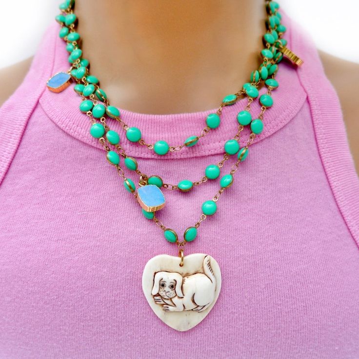 Handcrafted truly one-of-a-kind unique necklace, a vintage hand carved doggie on a heart shaped ox-bone pendant, little square shaped turquoise charms throughout, an evil eye a tiny moon sliver in pave crystals and a silk tassel all on a green vintage enamel chain measuring 38” long. Wear it long, doubled or tripled in any way creative way you like. Necklace is 38" in length Hand-carved heart pendant Variety of different charms Vintage enamel chain Made with love in Los Angeles Complimentary gif Green Vintage Charm Pendant Jewelry, Whimsical Green Pendant Jewelry, Green Pendant Jewelry With Vintage Charm, Green Bohemian Jewelry With Charms, Green Necklaces With Dangling Charms For Gifts, Green Necklaces With Dangling Charms As Gift, Green Necklace With Dangling Charms For Gift, Green Necklace With Dangling Charms As Gift, Whimsical Green Charms Jewelry