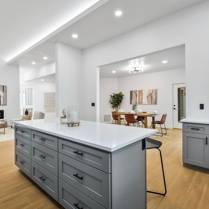 an open kitchen and living room with white walls, hardwood flooring and gray cabinets