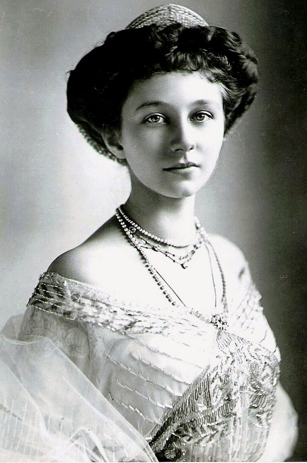 an old black and white photo of a woman in a dress with pearls on her head