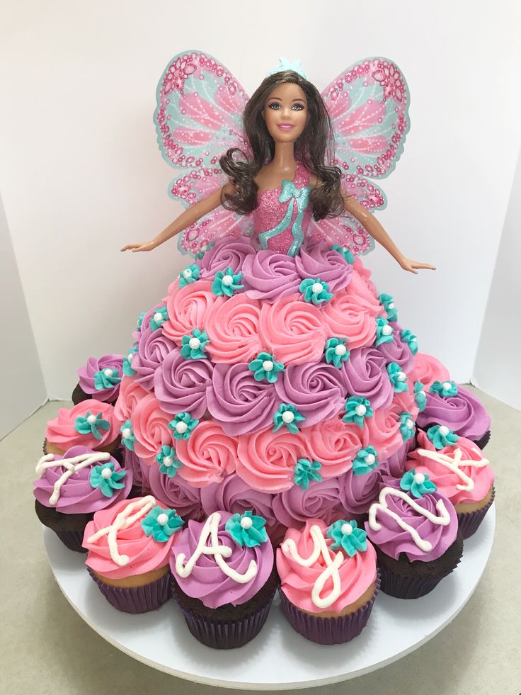 a barbie doll sitting on top of a cake with cupcakes