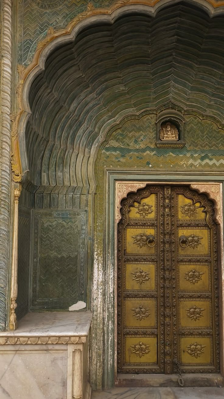 an ornate entrance to a building with gold doors and carvings on the walls, in front of a marble bench