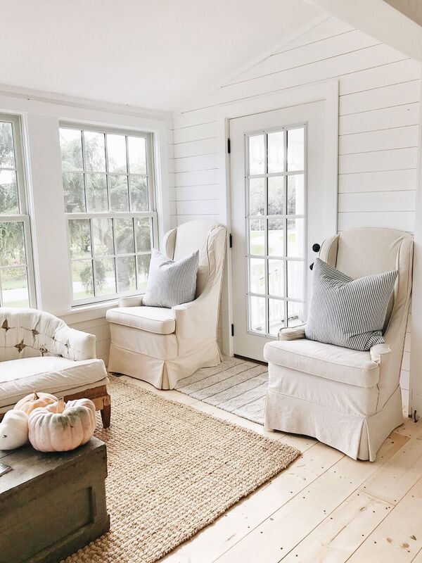 a living room filled with furniture and pillows on top of a wooden floor next to two windows