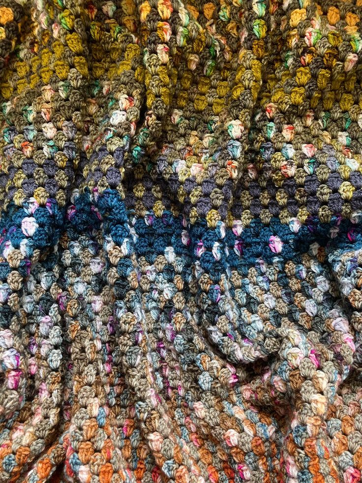 a multicolored crocheted blanket is laying on top of a tablecloth