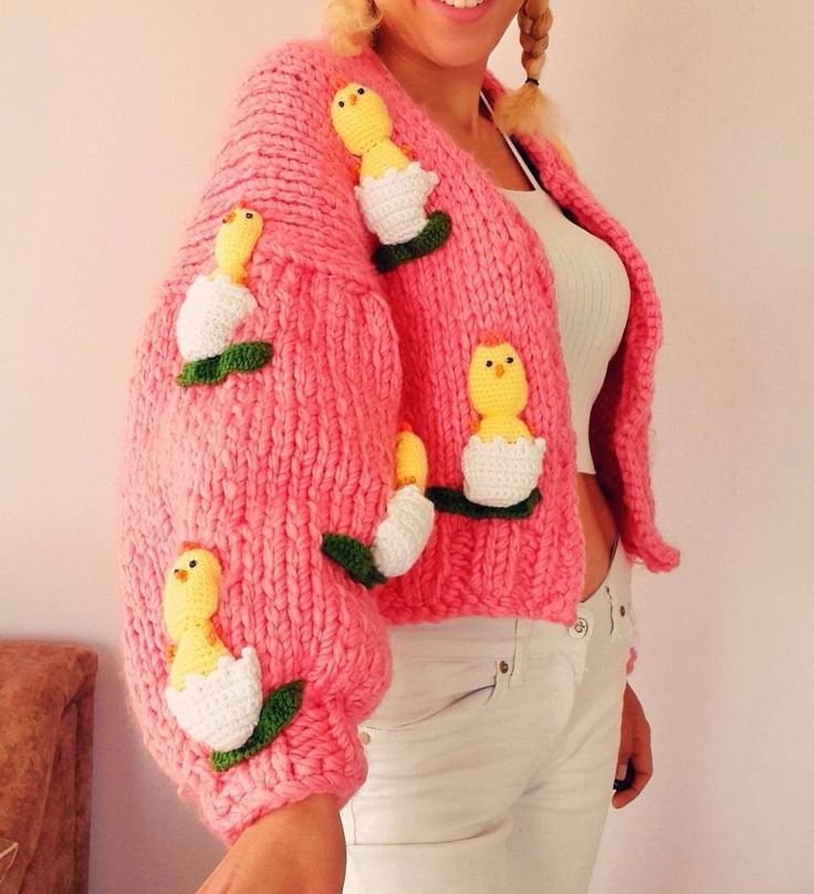 a woman wearing a pink knitted sweater with ducks on the front and sides, while standing next to a wall