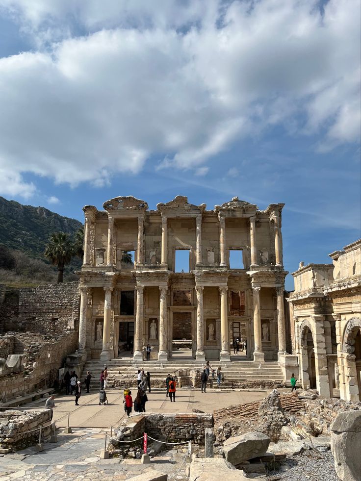 people are walking around in front of an old building with columns and arches on it