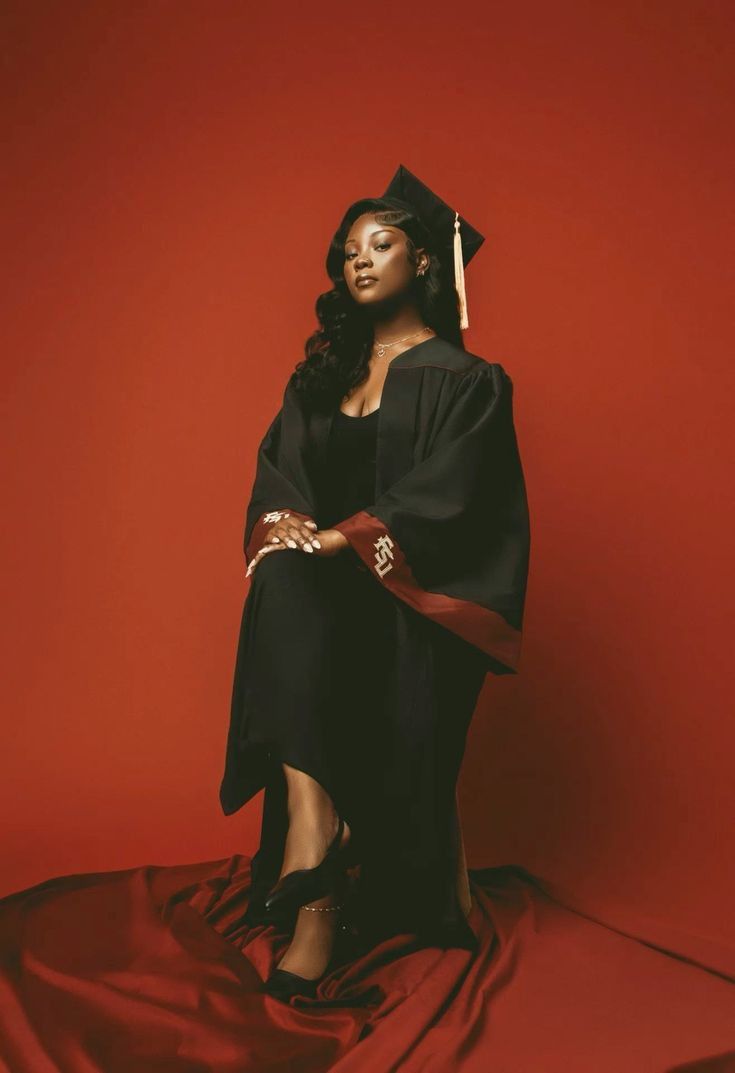 a woman in a graduation gown and cap posing for a photo on a red background