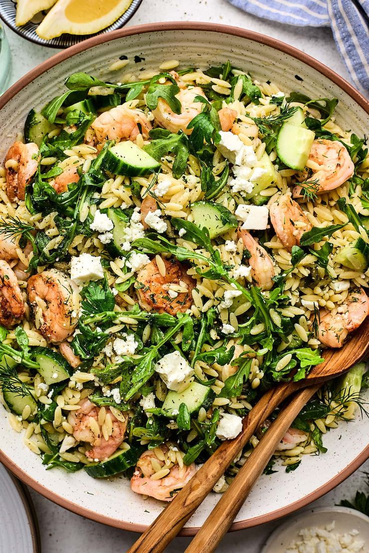 a salad with shrimp, spinach and feta cheese in a bowl next to two wooden chopsticks