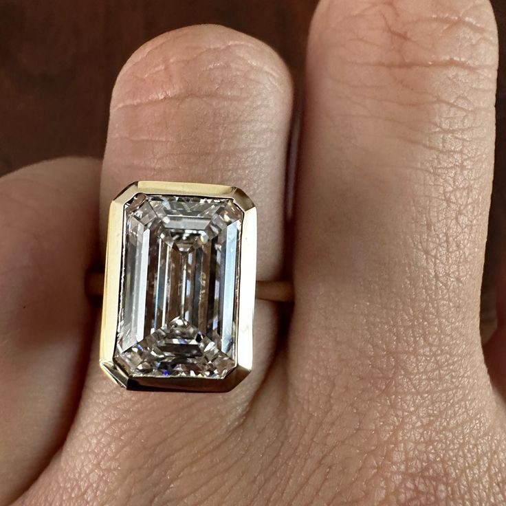 a close up of a person's hand holding a ring with an emerald stone