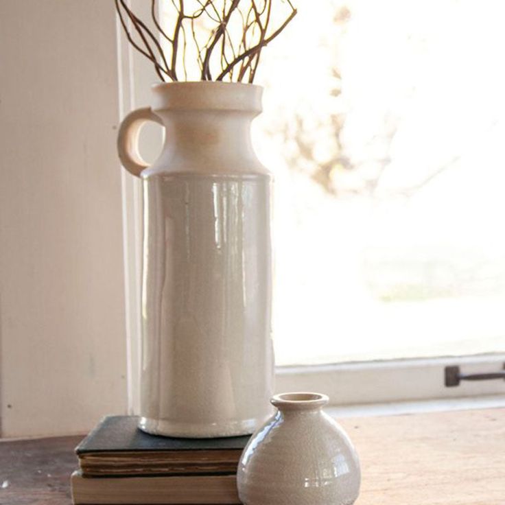 a white vase sitting on top of a wooden table next to a book and plant