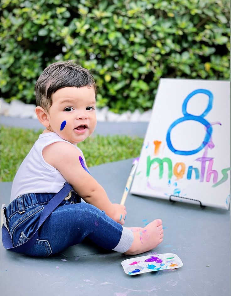 a little boy sitting on the ground with his feet up in front of an easel