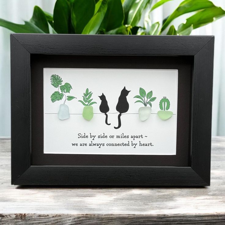 a black frame with some green plants and cats on the side, sitting in front of a potted plant