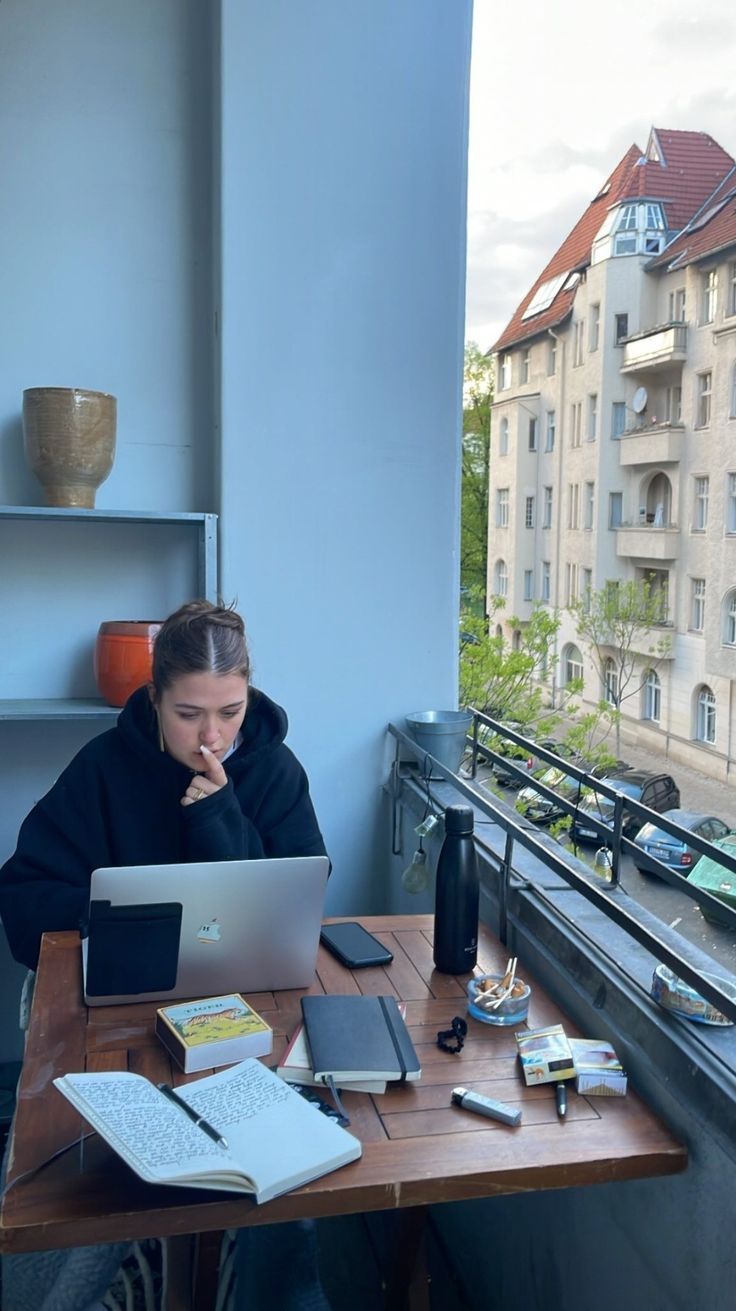 a woman sitting at a table with a laptop computer on her lap and looking out the window