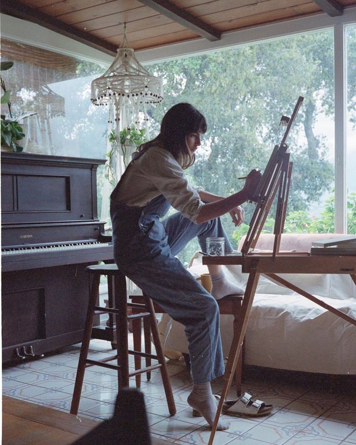 a woman sitting at a table with an easel and paintbrush in her hand