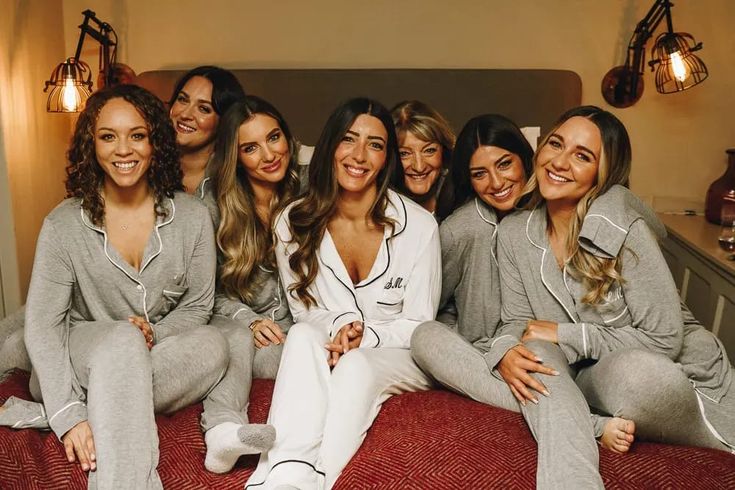 a group of women sitting on top of a bed wearing matching pajamas and pjss