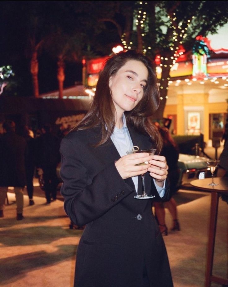 a woman in a black coat holding a wine glass