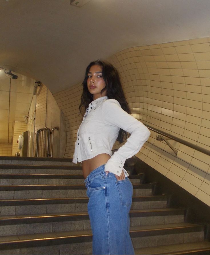 a woman standing in front of some stairs with her hands on her hips and looking at the camera