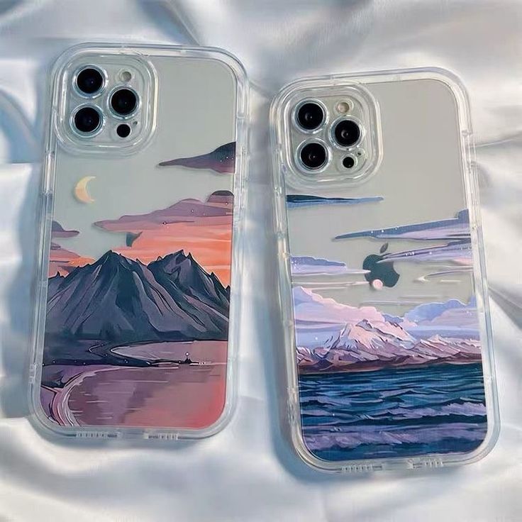 two iphone cases sitting on top of a white bed next to each other with mountains in the background