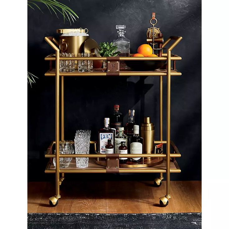 a bar cart with bottles and glasses on it in front of a potted plant