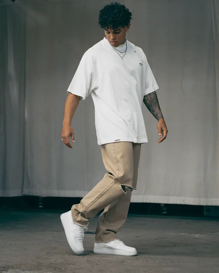 a man in white shirt and khaki pants walking with his foot on the ground