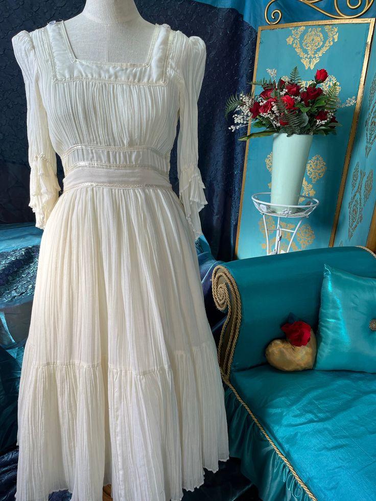 "Gunne Sax 1970 re-designed dress, ivory, crinkle cotton voile, cream, satin ribbon trim, beige, ribbed trim around neck line. 3/4 sleeve with double ruffles. The bodice has three lines of satin ribbon. The skirt is full, flowing, ballerina length it's an attached under slip. Size 7/8, bust 32\", waist 28\", waist to hem 33\". Washable" Cream Empire Waist Dress With Ruffles, Regency Style Cream Dress With Ruffles, Cream Vintage Dress With Ruffles For Formal Occasions, Cream Vintage Dress With Ruffles For Wedding, Cream Vintage Wedding Dress With Ruffles, Elegant Fitted Cream Prairie Dress, Cream Prairie Dress With Lace Trim For Wedding, Regency Victorian Dress With Ruffles In Cream, Elegant White Prairie Dress With Fitted Bodice