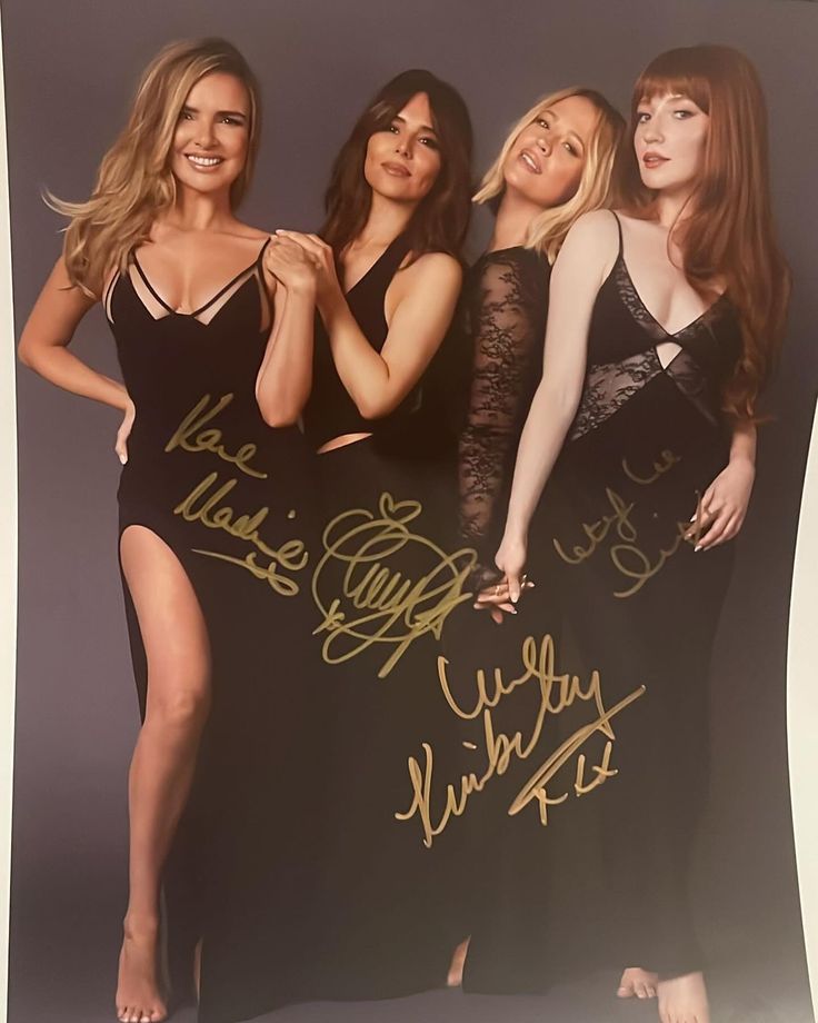 three beautiful women posing in front of a black backdrop with gold writing on it and one woman is holding her hand up to her chest