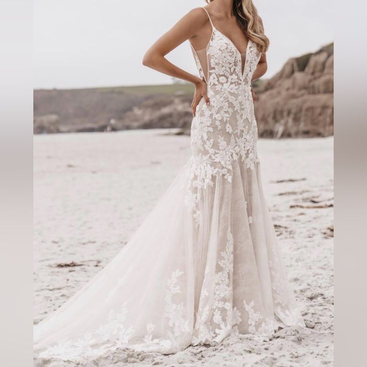 a woman standing on top of a sandy beach wearing a dress with white lace and flowers