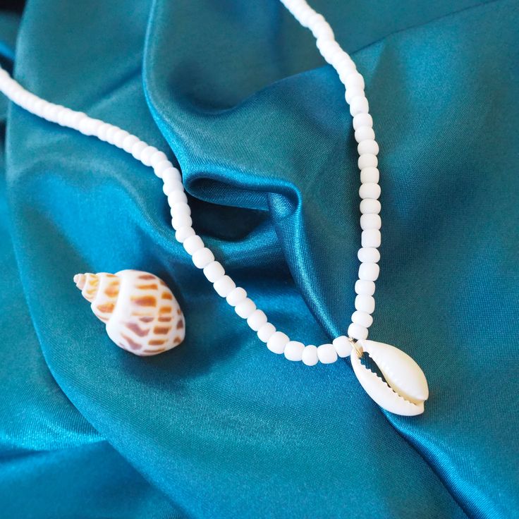 Introducing the Po'olenalena Layers Necklace – a charming duo inspired by the tranquil beauty of Po'olenalena Beach! This delightful layered necklace set brings a touch of the Hawaiian shores to your style. Wear them together for a stunning layered look or separately for a subtle island vibe. The first necklace features delicate white beads with a beautiful cowry shell centerpiece, perfect for adding a touch of elegance to your beachy ensemble. The second necklace is a string of enchanting cowry shells, capturing the essence of the ocean's treasures. Handcrafted with care, the Po'olenalena Layers Necklace is your go-to accessory for any sun-soaked adventure or tropical getaway. Embrace the spirit of the islands and let your inner beach lover shine! Seashells: real cowry White beads with lo White Beaded Clavicle Chain Necklace As Gift, White Shell Charm Necklace As Gift, White Shell Charm Necklace Gift, White Shell Charm Necklace For Gift, White Shell Charm Necklaces For The Beach, White Summer Beach Charm Necklaces, White Shell-shaped Necklace For A Gift, White Shell-shaped Necklace For Gift, White Shell Charm Necklaces