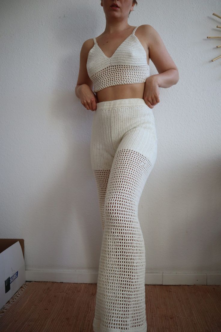 a woman in white pants and crop top posing for the camera with her hands on her hips