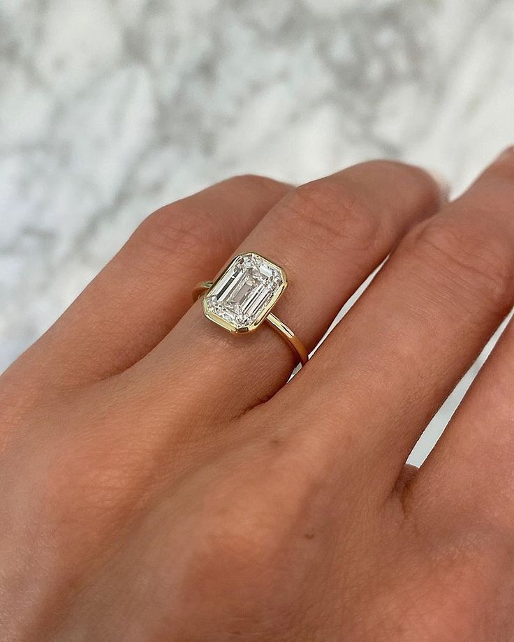 a woman's hand with a diamond ring on top of her finger, in front of a marble background