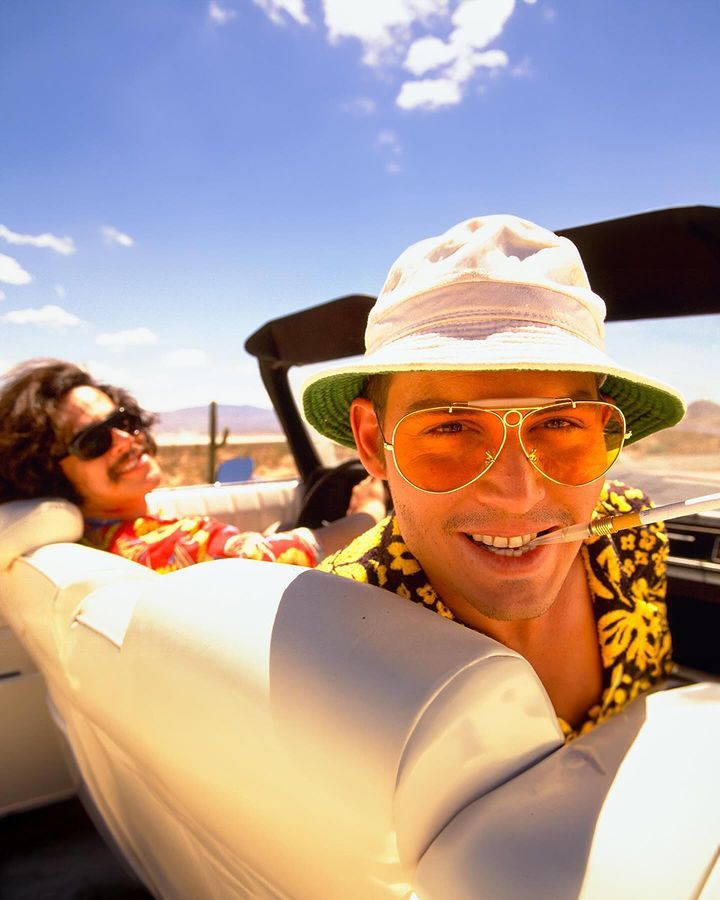 a man in sunglasses and a hat sitting in the back of a white convertible car