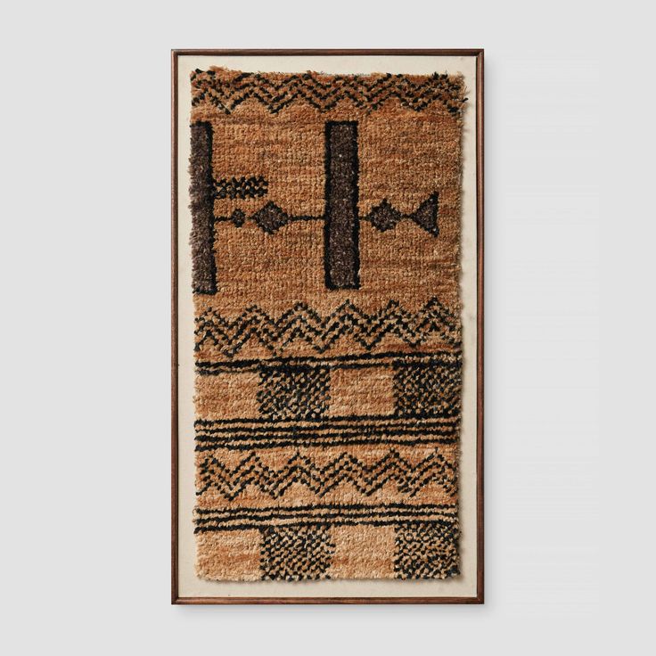 a brown and black rug hanging on a wall next to a wooden framed artwork piece