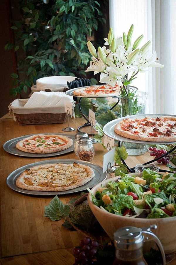 a wooden table topped with lots of pizzas next to a vase filled with flowers