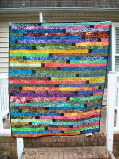 a multicolored quilt hanging on the side of a house in front of a porch