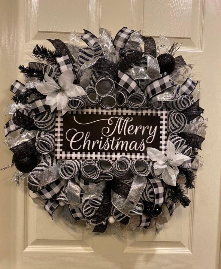 a christmas wreath with black and white bows hanging on the front door to say merry christmas