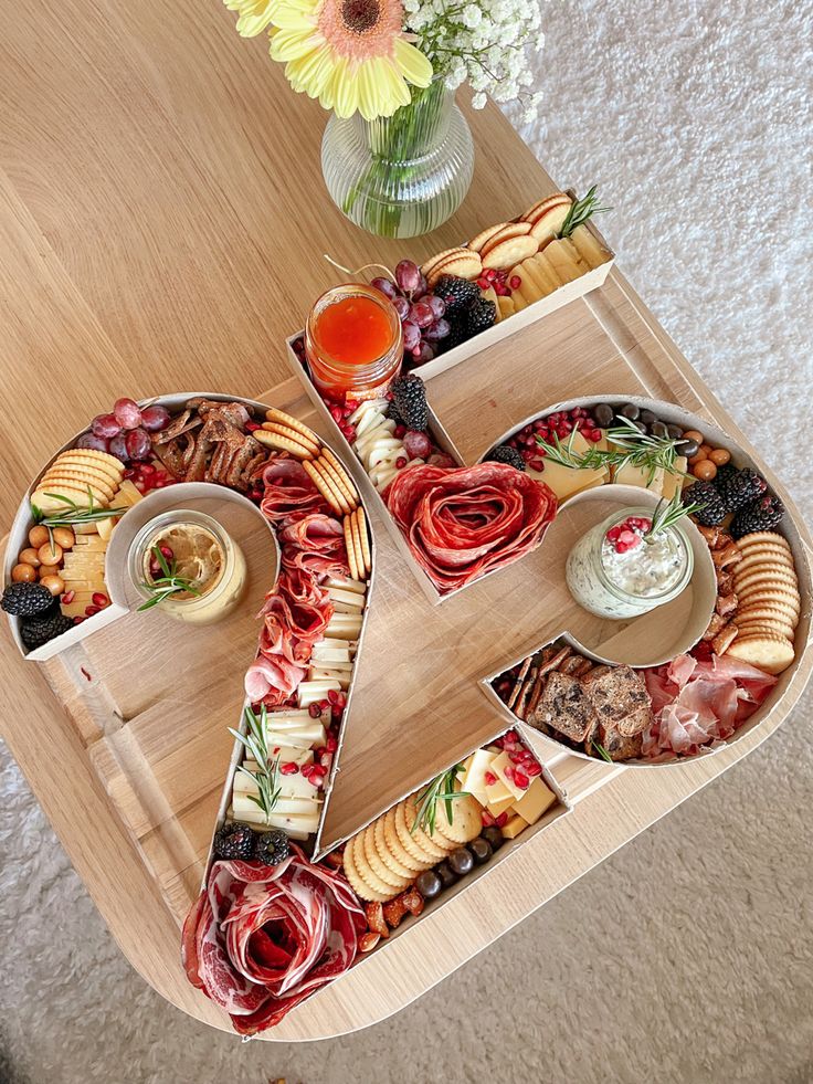 a wooden table topped with plates and trays filled with different types of food next to a vase full of flowers