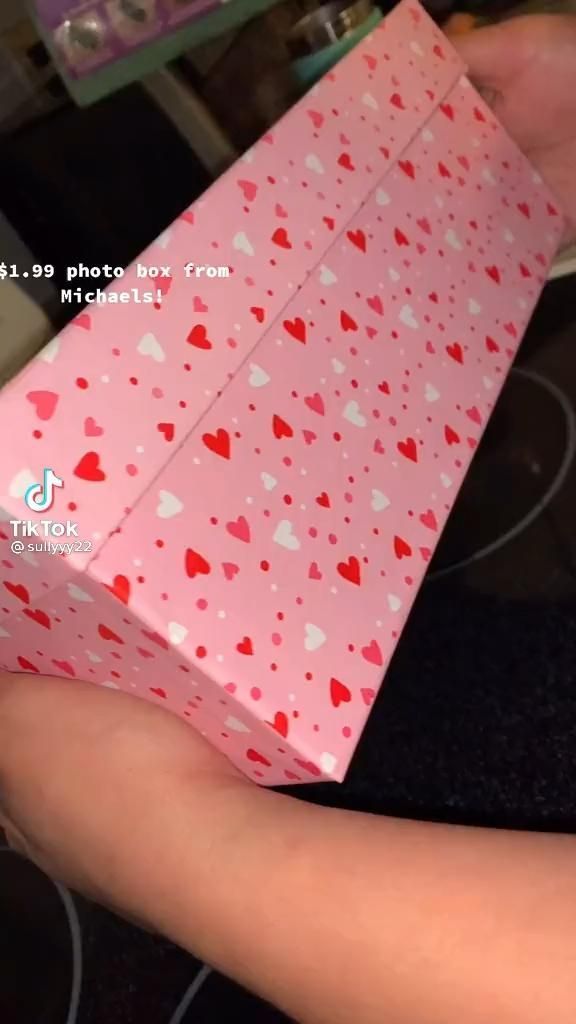 someone holding a pink gift box with hearts on it