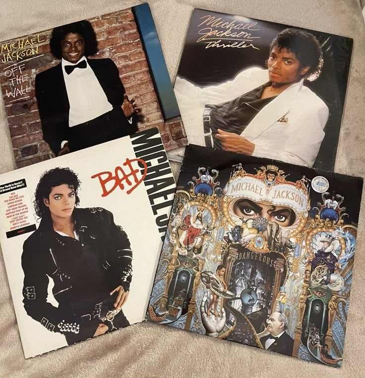 four different album covers are laying on a white sheet and one has an image of michael jackson