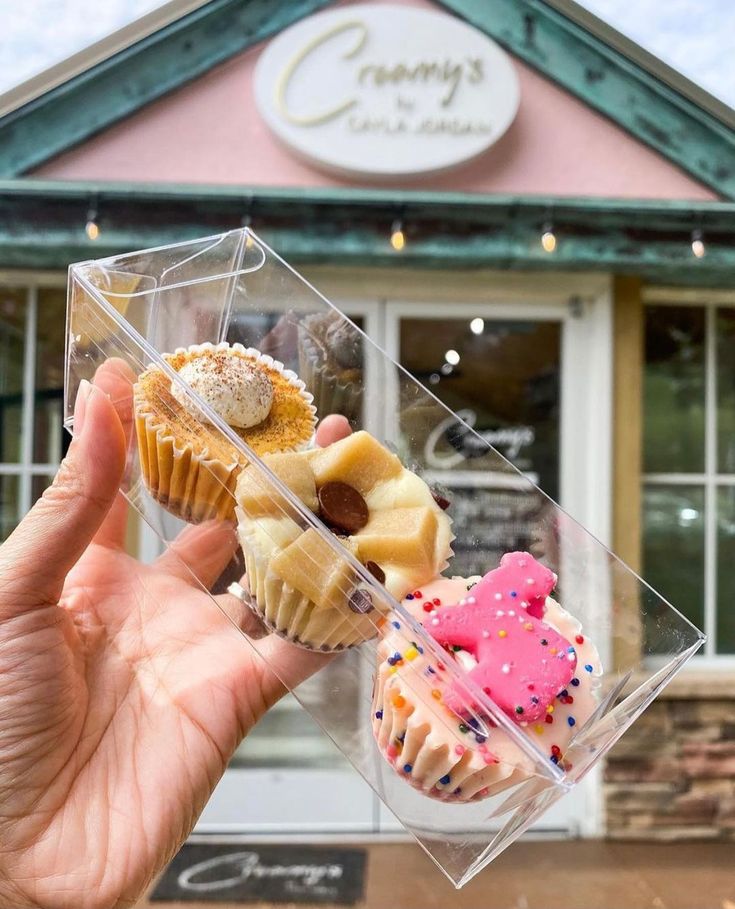 a person holding up a cupcake in front of a building with donuts on it