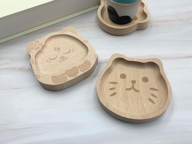 two wooden coasters with cat faces on them, one has a coffee cup in the middle