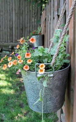 some orange flowers are growing in a metal pot on the side of a wooden fence