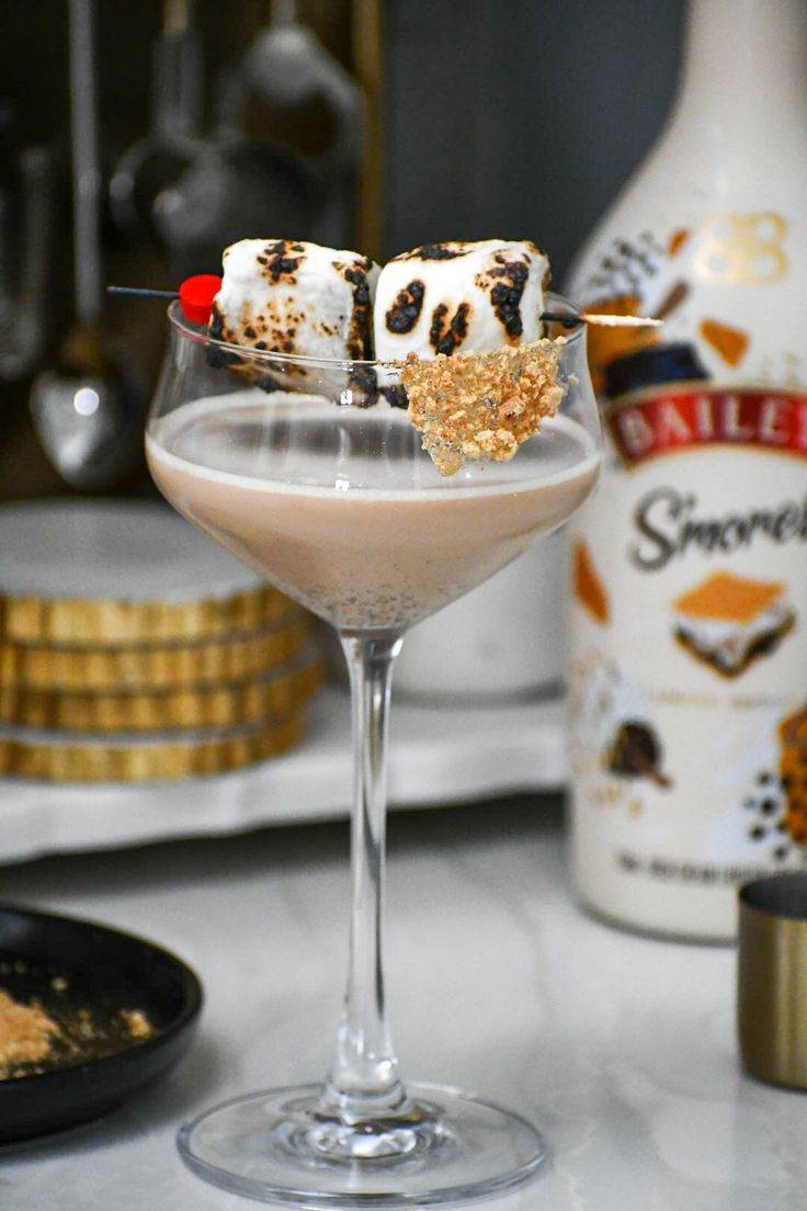 a dessert in a wine glass on a table with other food and drink bottles behind it