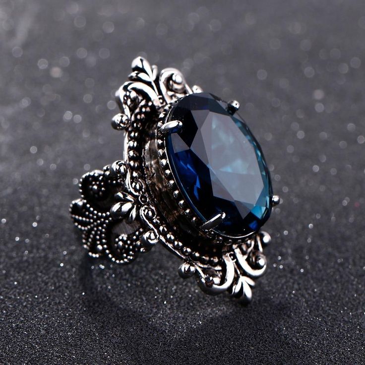 This gorgeous sterling silver ring is perfect for a person with a flare for vintage jewelry. The Blue Sapphire Peacock Vintage Ring features an oval blue sapphire as its centerpiece, encircled by small round white diamonds that catch the light gloriously and radiate life! From cornflower blue to velvety blue, there are multifarious shades of blue sapphire that gives it a silky tint. Characterized by the power of Shani or Saturn, Blue Sapphire displays violet to indigo and pale blue as well as da Elegant Silver Sapphire Oval Ring, Elegant Oval Sapphire Ring In Silver, Victorian Style Oval Sapphire Ring, Elegant Silver Sapphire Ring In Oval Shape, Victorian Oval Sapphire Ring, Elegant Sapphire Crystal Ring, Elegant Blue Oval Crystal Ring, Victorian Sapphire Oval Rings, Vintage Sapphire Ring Jewelry