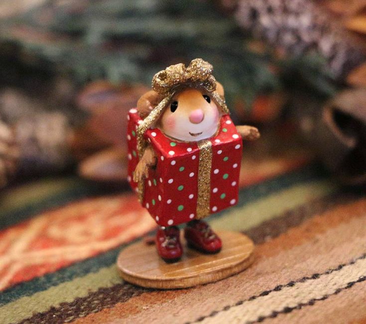 a small figurine is standing on a wooden stand with a red present in it's hand