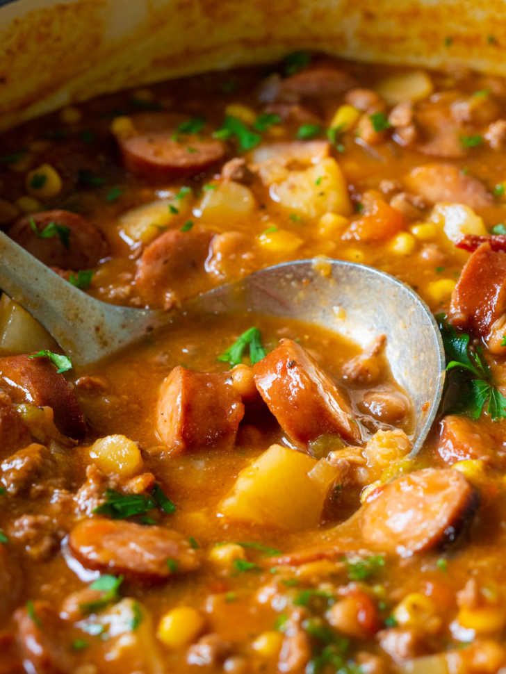 a bowl of soup with sausage, potatoes and carrots in it is being stirred by a spoon