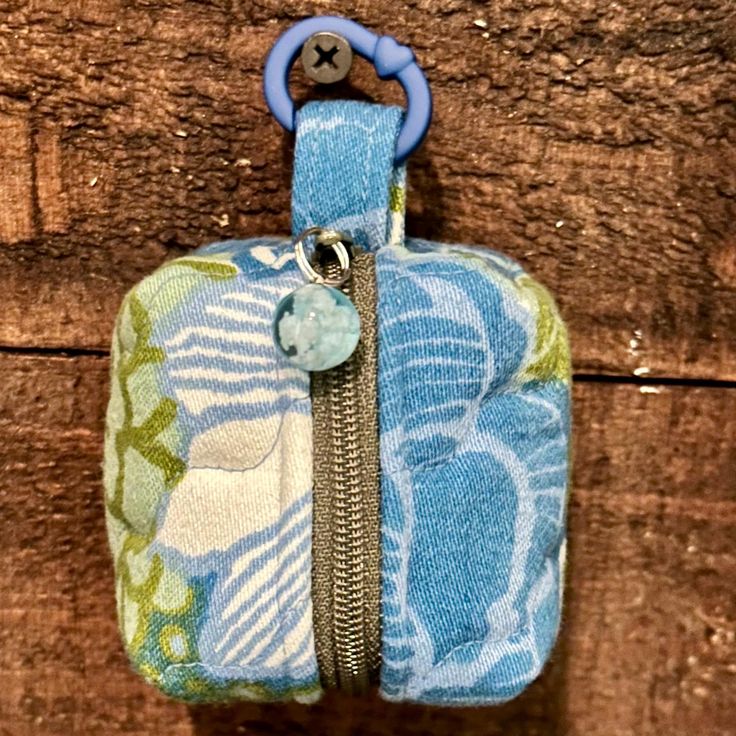 a blue and green purse hanging on a wooden wall with a keychain attached to it