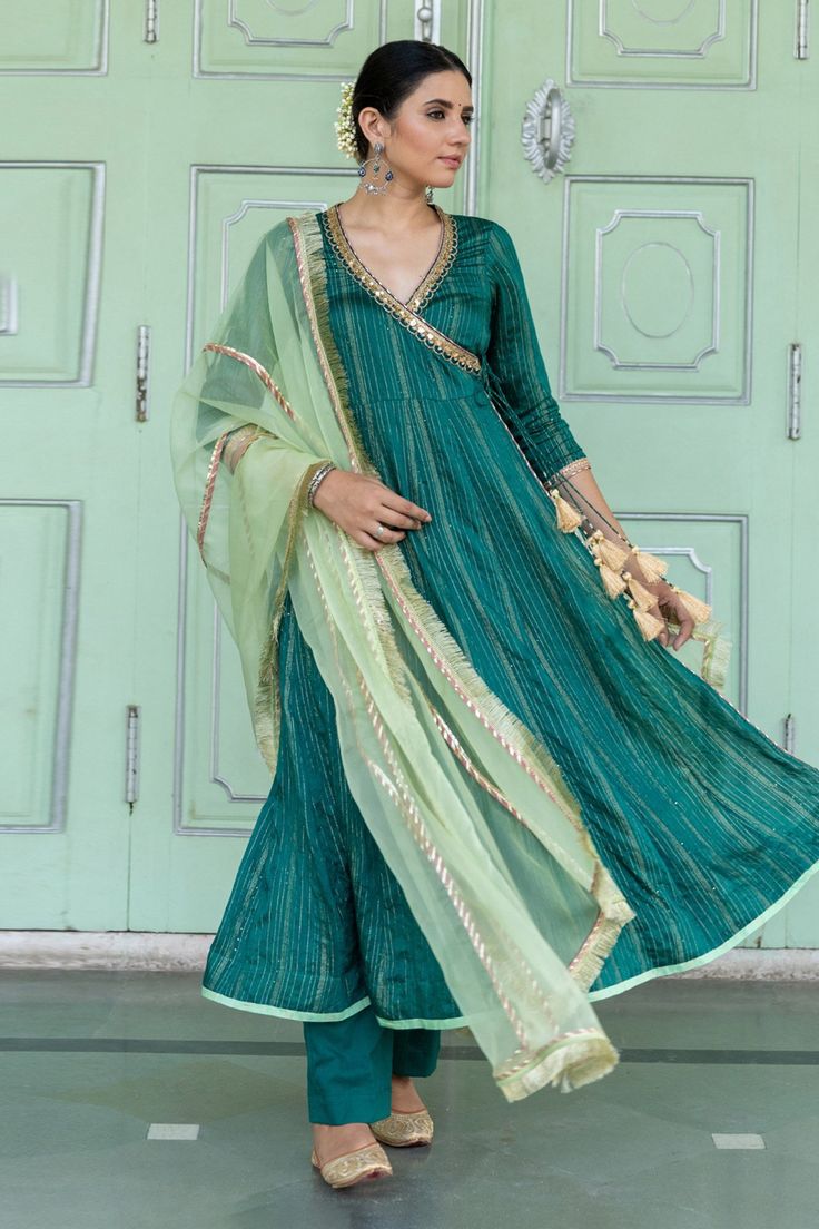 Emerald green chanderi blend angarkha with intricate sequin details, overlap panel and lace work. Paired with pants and blue light green organza dupatta with fringe lace border.
Component: 3
Pattern: Embroidered
Type Of Work: Gota and Sequin Work
Neckline: Surplice Neck
Sleeve Type: Three Quarter
Fabric: Angarkha: Chanderi Blend, Dupatta: Organza
Color: Green
Other Details: 
Side tassel tie-up on kurta
Gota work details on dupatta
Occasion: Puja,Haldi and Mehendi - Aza Fashions Green Raw Silk Anarkali Set For Navratri, Green Chanderi Choli For Transitional Season, Green Anarkali Dupatta For Transitional Season, Green Art Silk Anarkali Set, Transitional Green Anarkali Set In Art Silk, Designer Green Choli With Straight Kurta, Green Art Silk Anarkali Set For Designer Wear, Green Anarkali Set With Gota Work For Navratri, Designer Green Art Silk Anarkali Set