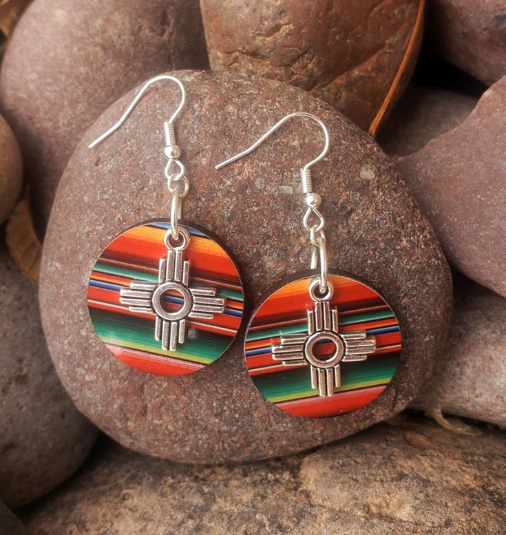 Zia Round Serape Earrings, New Mexico Serape Earrings, Southwestern Earrings, Western Earrings, Zia Jewelry, New Mexico Jewelry.  These lightweight earrings are perfect statement of the Southwest.  Earring is a lightweight wood printed with a vibrant serape print.  Final touch to adorn these precious earrings is a stainless-steel Zia charm.  These will for sure be your favorite earrings.  Perfect with any outfit and so light you won't even remember you are wearing them.  Get your today, they com New Mexico Jewelry, Concho Dangle Earrings For Gift, Festival Concho Dangle Jewelry, Adjustable Concho Earrings For Festival, Multicolor Southwestern Teardrop Jewelry, Multicolor Southwestern Style Teardrop Jewelry, Southwestern Style Multicolor Teardrop Jewelry, Southwestern Teardrop Jewelry For Festivals, Southwestern Red Dangle Earrings