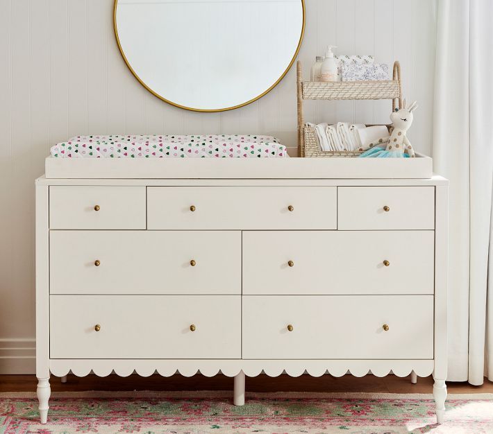 a white dresser with a mirror above it and a baby crib in the background