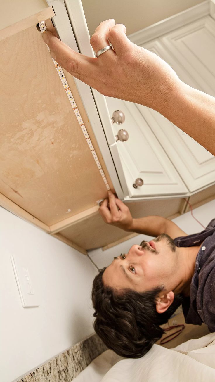 a man is trying to fix the cabinet door on his kitchen counter top, while he looks up