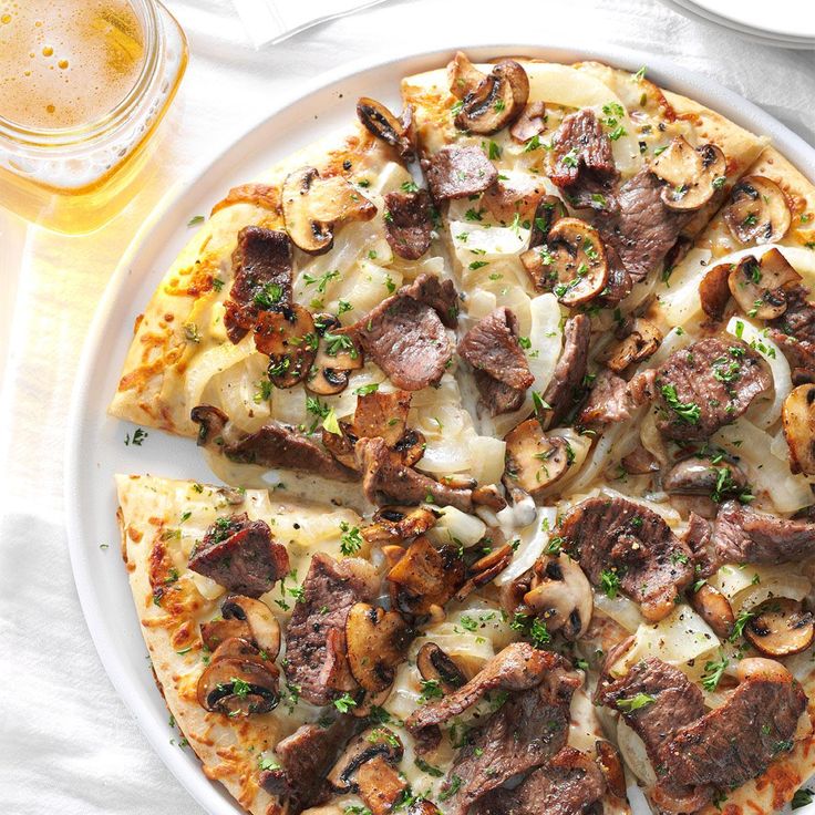 a pizza sitting on top of a white plate covered in toppings next to a glass of beer